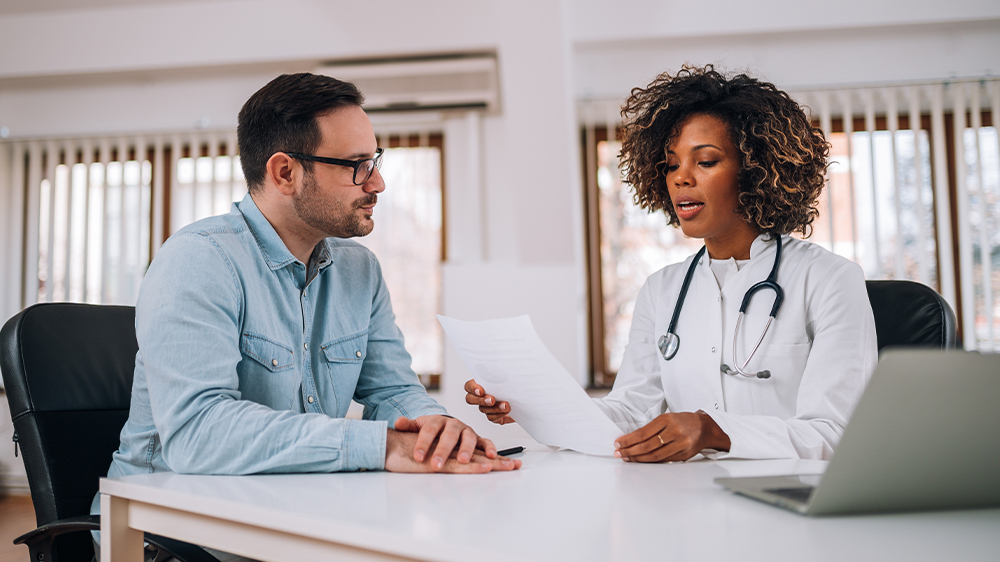 A male patient sitting with a female physician reviewing a document that may cover common male fertility problems.