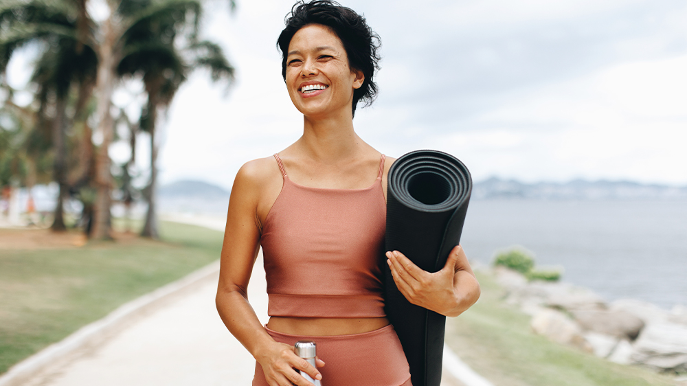 A smiling couple jogs in nature on a sunny day, potentially trying an activity that could help increase ovulation naturally.
