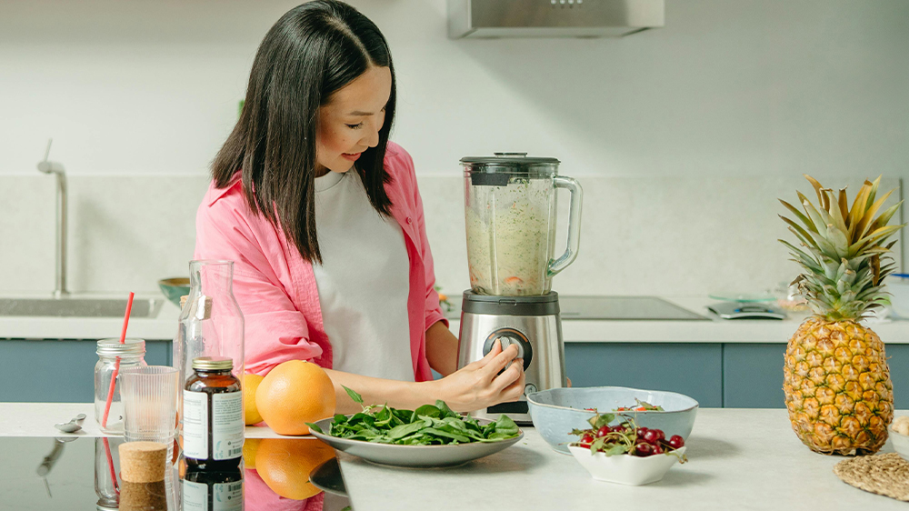 A woman operates a blender full of ingredients that could be for a fertility smoothie, like spinach and fruits.